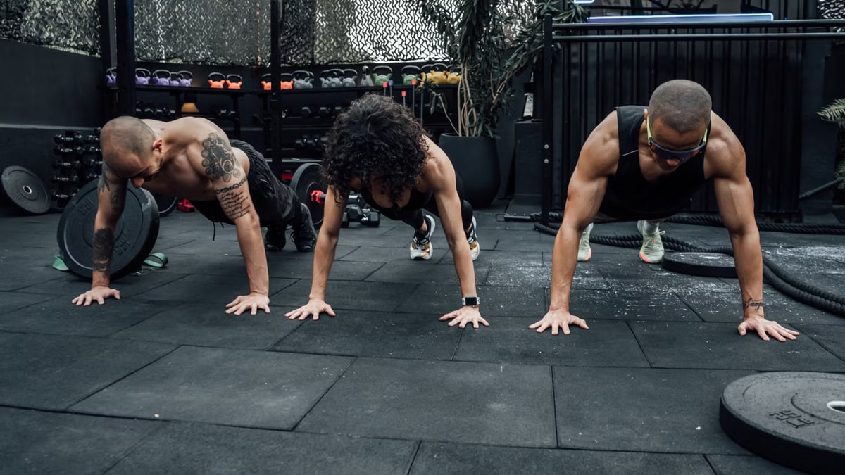 Three individuals performing push-ups together in a Mexico City gym setting.